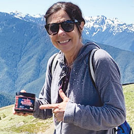 Photo of AIM Member Char Pelfrey holding AIM Peak Endurance product with mountains in the background